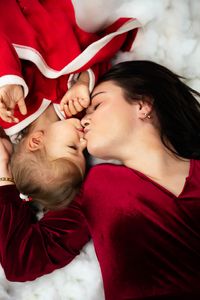 &quot;Mutter und Tochter in roten Weihnachtsoutfits k&uuml;ssen sich liebevoll auf einem Weihnachtsfotoshooting, das auf aufgebauter Watte wie Schnee inszeniert ist. Das Foto wurde von Pongratz Photography gemacht.&quot;