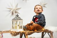 Glückliches 1-jähriges Kind in weihnachtlich beleuchtetem Schlitten, schaut nach oben, umgeben von Sternen, Weihnachtsfotoshooting in Kaufbeuren