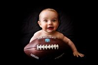&quot;Ein lachendes Baby liegt auf einem Football. Im Hintergrund ist eine schwarze Leinwand zu sehen. Das Foto wurde von Pongratz Photography in einem mobilen Fotostudio in Kaufbeuren aufgenommen.&quot;