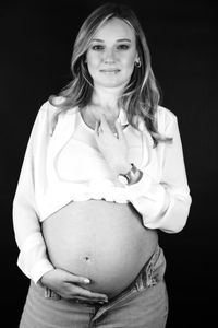 Eine strahlende, schwangere Frau, die vor einem mobilen Fotostudio in Kaufbeuren gl&uuml;cklich posiert. Das Foto ist in schwarz wei&szlig;.