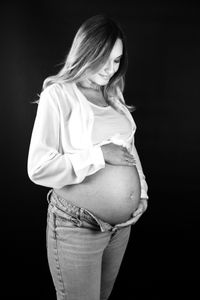 Eine strahlende, schwangere Frau, die vor einem mobilen Fotostudio in Kaufbeuren gl&uuml;cklich posiert. Das Foto ist in schwarz wei&szlig;.