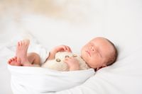 Neugeborenes Baby schl&auml;ft friedlich in wei&szlig;em Strampler auf wei&szlig;em Hintergrund, Boho-Stil Babyfotografie Kaufbeuren von Pongratz Photography