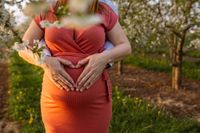 Schwangere und Partner formen Herz &uuml;ber Babybauch, Kirschbl&uuml;ten, Sonnenuntergang, romantische Schwangerschaftsfotografie Kaufbeuren